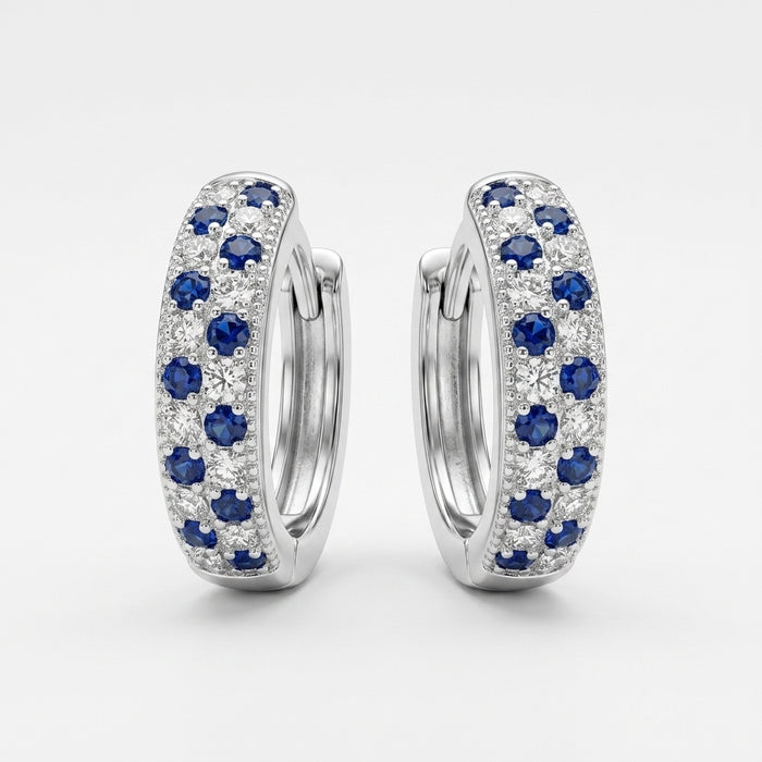 A pair of silver huggie hoop earrings adorned with rows of round-cut blue sapphires and clear pavé diamonds, set against a clean white background.