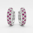 A pair of silver huggie hoop earrings decorated with pavé-set pink gemstones and small clear stones, shown against a light gray background.