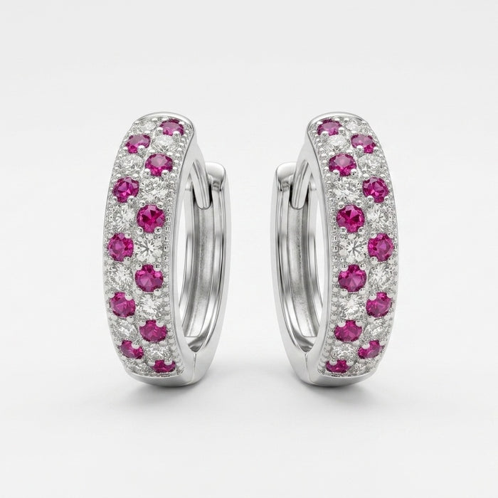 A pair of silver huggie hoop earrings decorated with pavé-set pink gemstones and small clear stones, shown against a light gray background.