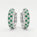 A pair of silver huggie hoop earrings set with round green emeralds and small clear stones, photographed on a clean white background.