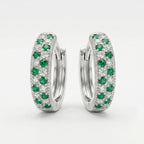 A pair of silver huggie hoop earrings set with round green emeralds and small clear stones, photographed on a clean white background.
