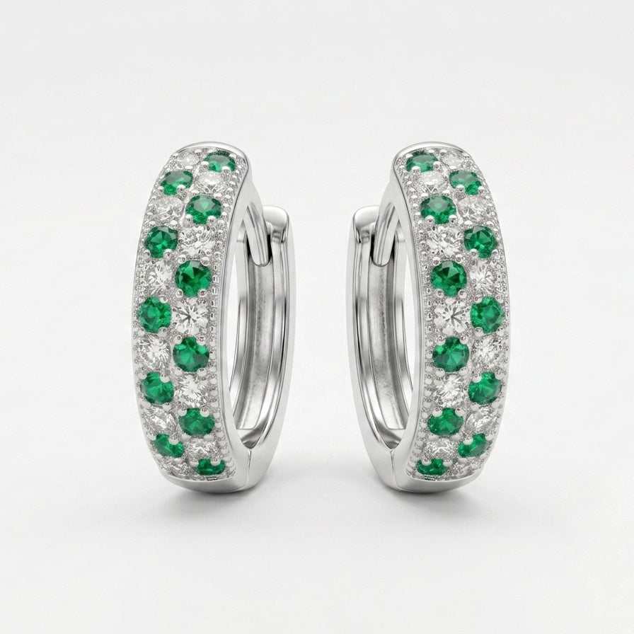 A pair of silver huggie hoop earrings set with round green emeralds and small clear stones, photographed on a clean white background.