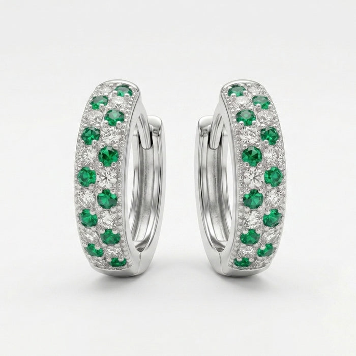 A pair of silver huggie hoop earrings set with round green emeralds and small clear stones, photographed on a clean white background.