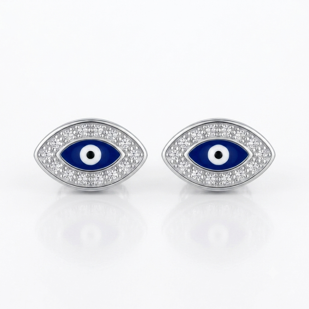 A pair of silver-toned evil eye stud earrings with blue enamel and white accents, set with small clear stones, on a white reflective background.
