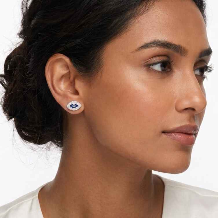 A close-up of a woman wearing a small white and blue evil eye stud earring, shown in profile against a clean white background.