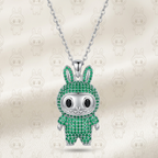 A silver bunny pendant necklace encrusted with green stones, hanging from a silver chain against a cream satin background with faint repeating bunny motifs.