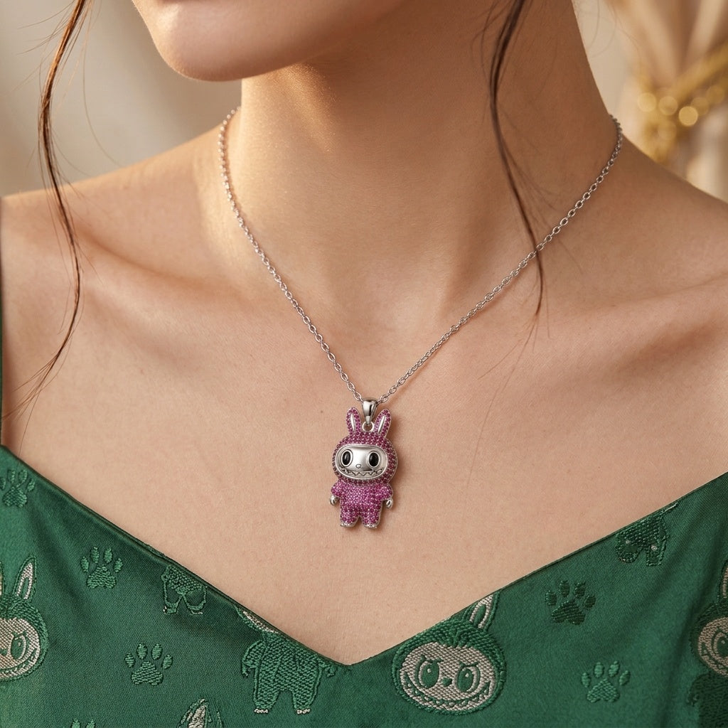 A close-up of a model wearing a silver chain necklace with a small cartoon bunny pendant. The pendant is decorated with pink rhinestones and a white face.