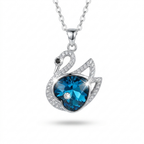 A silver-tone swan pendant necklace featuring a large faceted blue heart-shaped gemstone, surrounded by smaller clear crystals, on a white background.