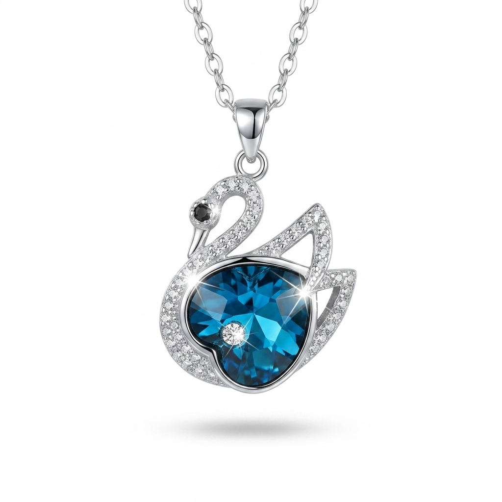 A silver-tone swan pendant necklace featuring a large faceted blue heart-shaped gemstone, surrounded by smaller clear crystals, on a white background.