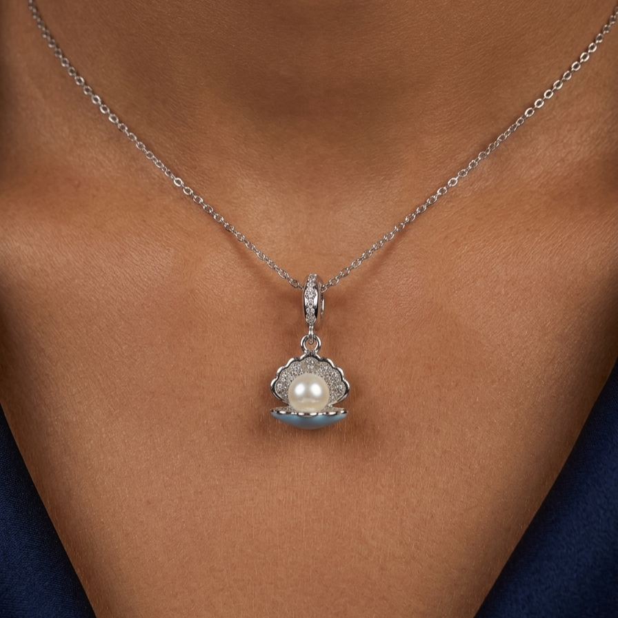 A silver chain necklace with a clam-shell pendant featuring a white pearl and light blue enamel, shown worn on a model's neck.