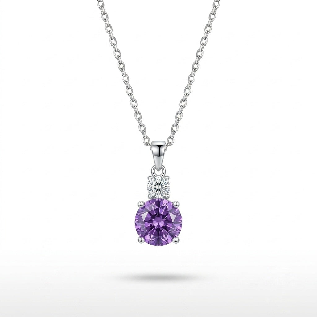 A silver pendant necklace featuring a round-cut purple amethyst gemstone in a four-prong setting, accented by a small cluster of clear stones above, suspended from a delicate silver chain against a white background.