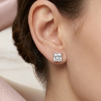 A close-up of a model's ear wearing a single princess-cut clear gemstone stud earring in a silver setting.