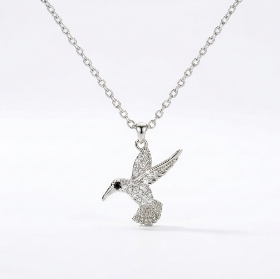 A silver-toned necklace featuring a detailed hummingbird pendant adorned with small clear stones, set against a clean white background.