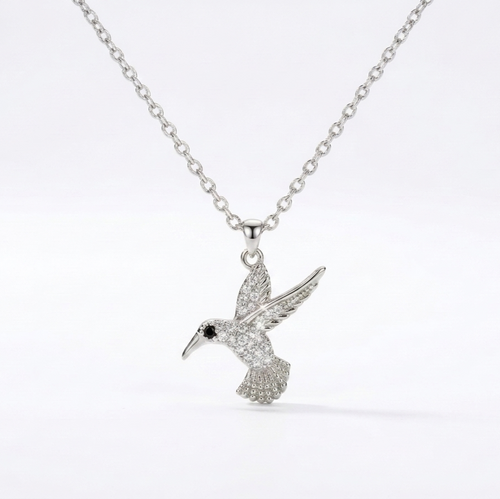A silver-toned necklace featuring a detailed hummingbird pendant adorned with small clear stones, set against a clean white background.