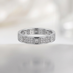 A silver-toned eternity ring set with round diamonds, suspended against a soft, out-of-focus white background.