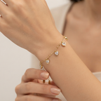 A delicate gold chain bracelet with three heart-shaped crystal charms worn on a woman's wrist, shown in a close-up lifestyle shot.