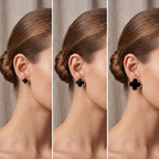Three close-up side views of a woman wearing a black clover-shaped stud earring with a gold-tone border. The model's hair is pulled back into a bun, and the background is a soft neutral curtain.