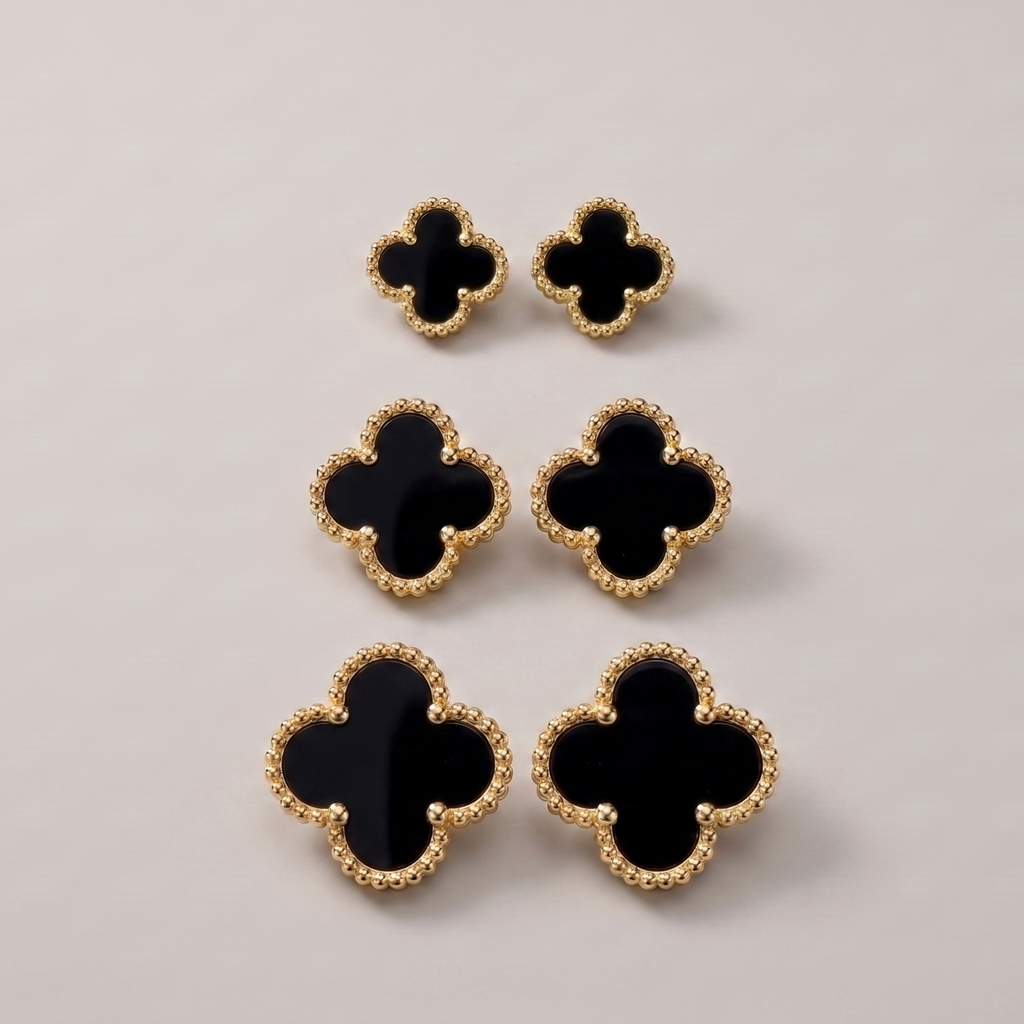 Six black clover-shaped earrings with textured gold borders, arranged in a vertical stack on a light gray background.