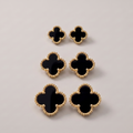 Six black clover-shaped earrings with textured gold borders, arranged in a vertical stack on a light gray background.