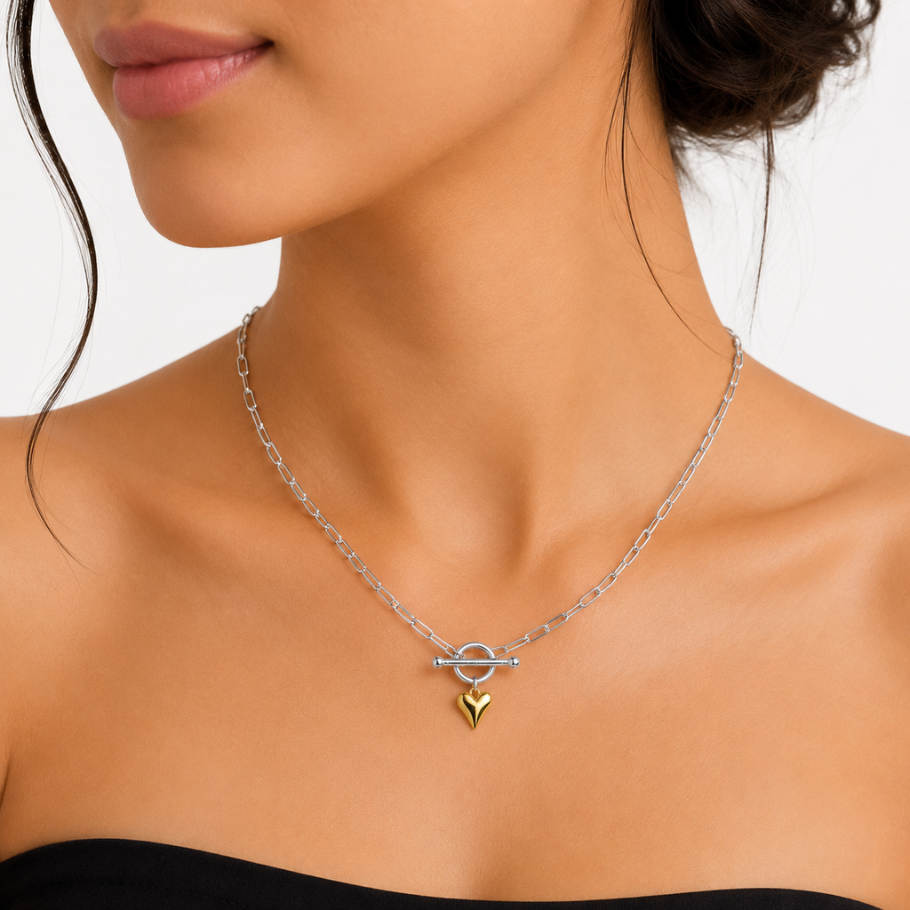 A close-up of a model wearing a delicate silver chain necklace with a toggle clasp and a small gold heart pendant.