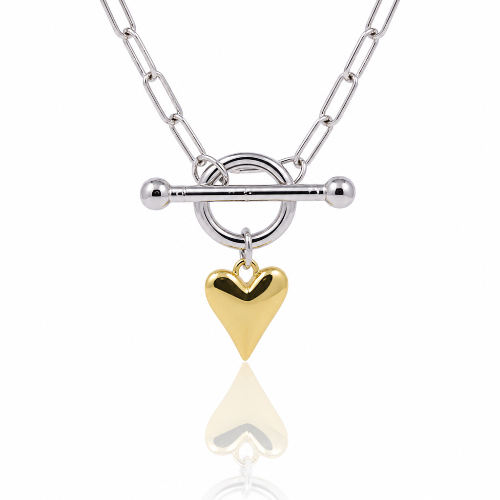 A silver chain necklace with a toggle clasp and a dangling polished gold heart charm, shown on a clean white background with a soft reflection below.