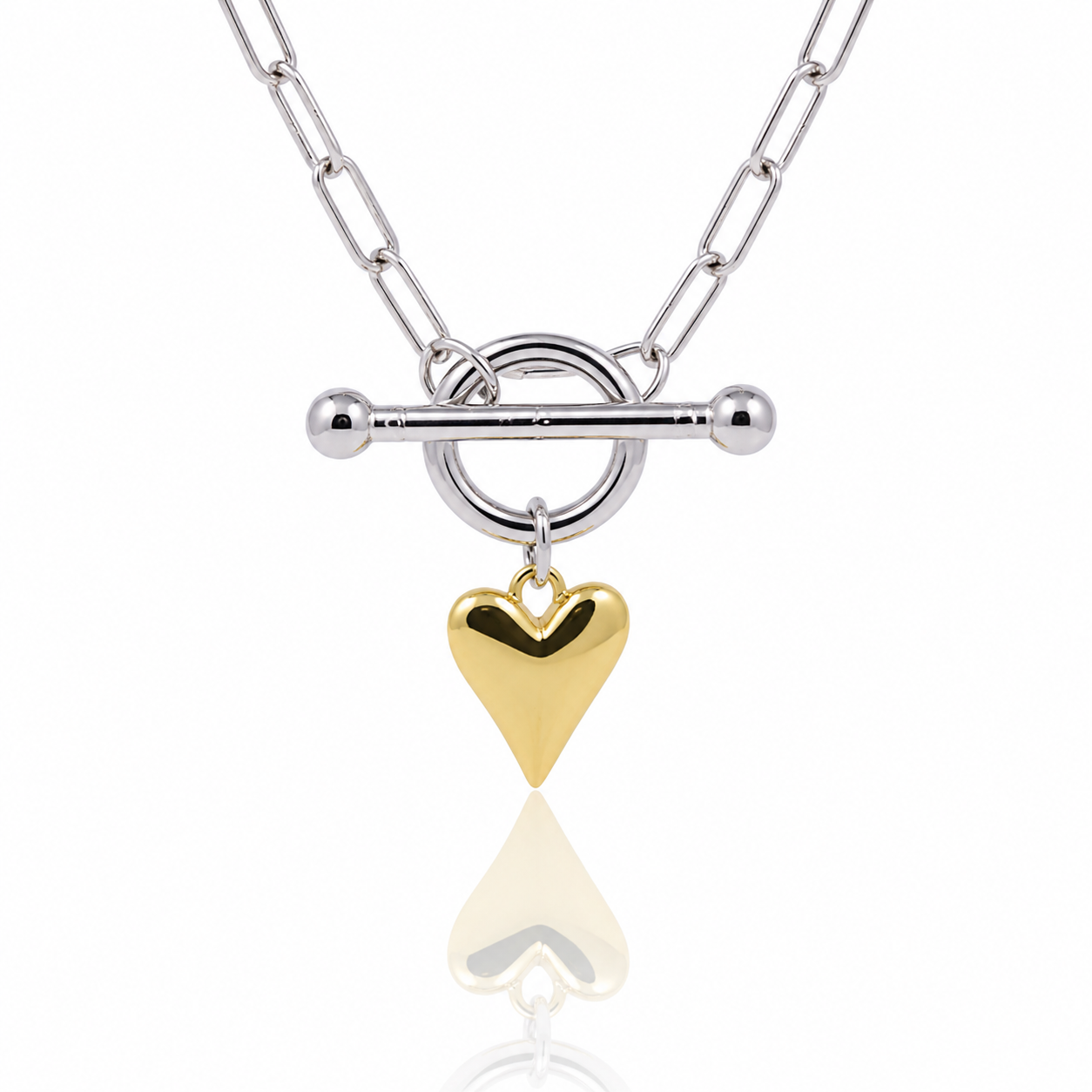 A silver chain necklace with a toggle clasp and a dangling polished gold heart charm, shown on a clean white background with a soft reflection below.