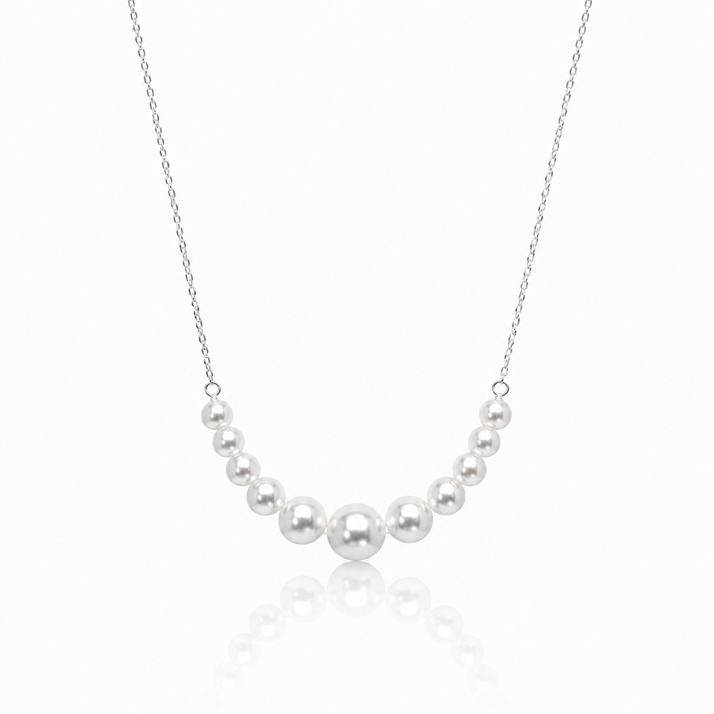 A delicate silver chain necklace featuring a curved row of seven white freshwater pearls of varying sizes, displayed against a clean white background with a soft reflection below.