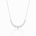 A delicate silver chain necklace featuring a curved row of seven white freshwater pearls of varying sizes, displayed against a clean white background with a soft reflection below.