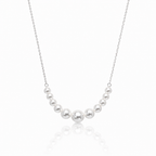 A delicate silver chain necklace featuring a curved row of seven white freshwater pearls of varying sizes, displayed against a clean white background with a soft reflection below.