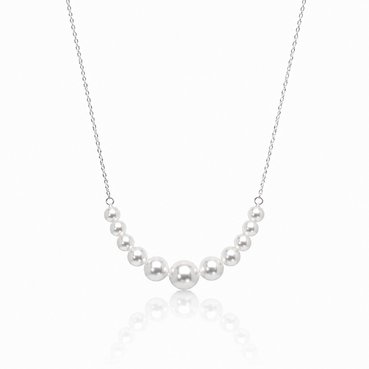 A delicate silver chain necklace featuring a curved row of seven white freshwater pearls of varying sizes, displayed against a clean white background with a soft reflection below.