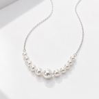 A delicate silver chain necklace featuring a graduated row of white freshwater pearls, displayed on a clean white surface.