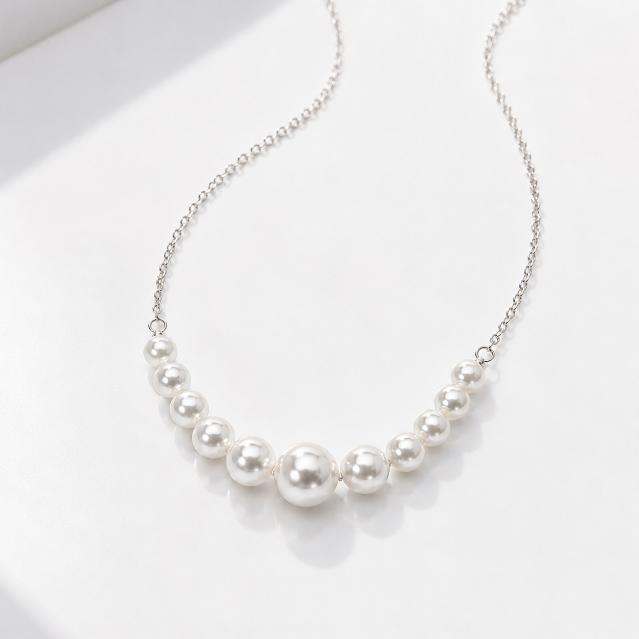 A delicate silver chain necklace featuring a graduated row of white freshwater pearls, displayed on a clean white surface.