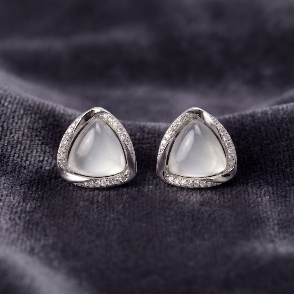 Pair of silver earrings with triangular gemstones on a dark fabric background