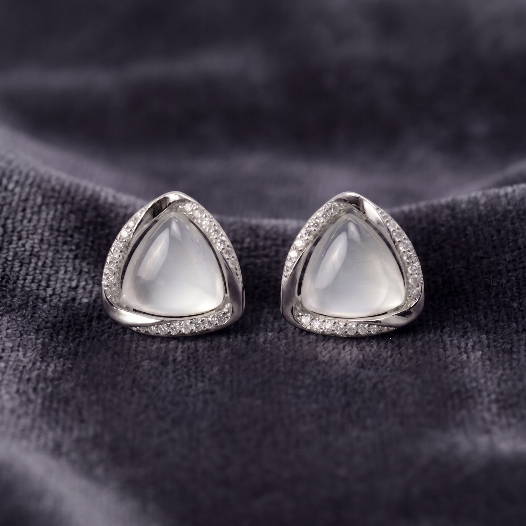 Pair of silver earrings with triangular gemstones on a dark fabric background