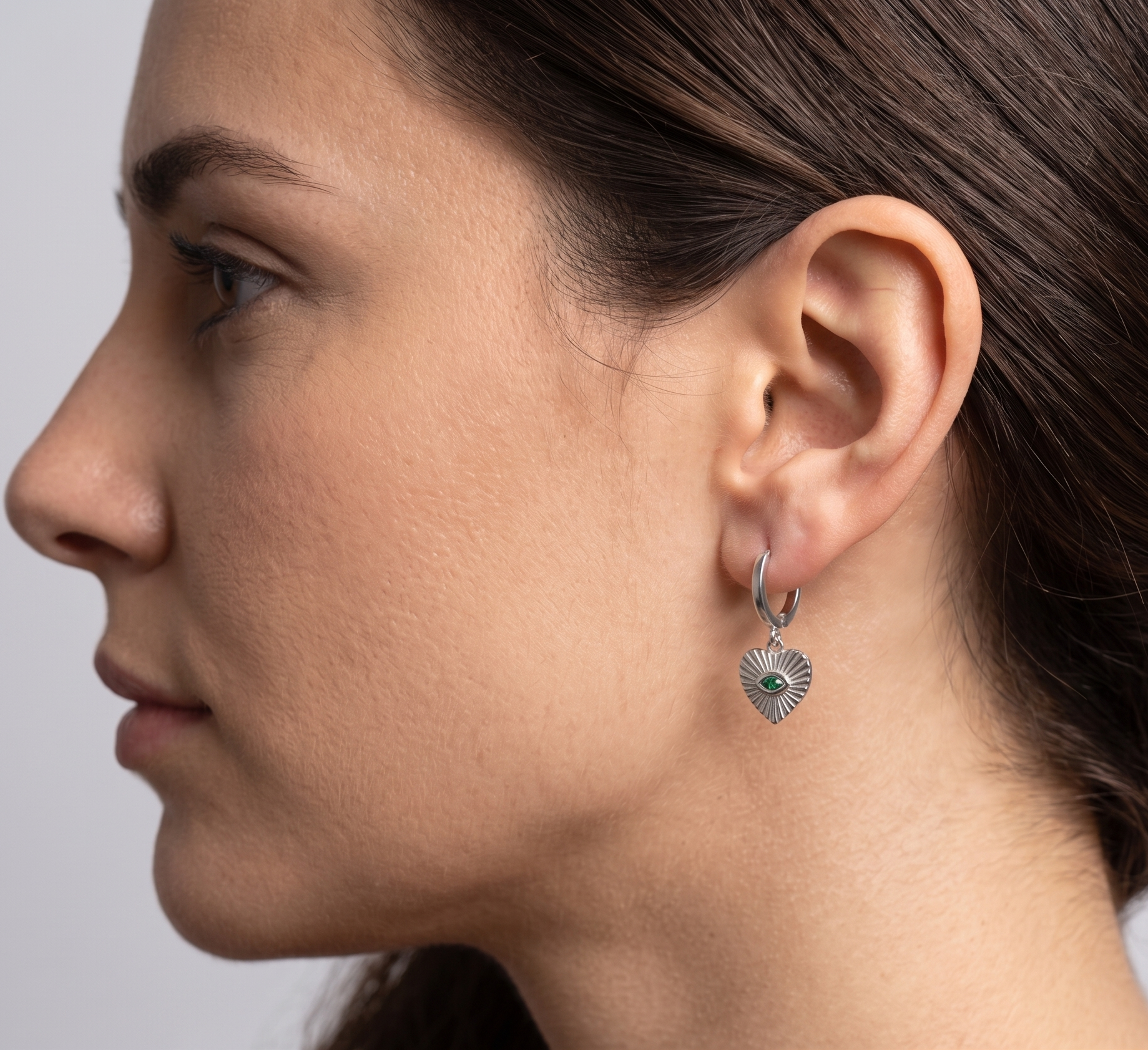 Close-up of a woman wearing a silver earring with a green gemstone on a neutral background