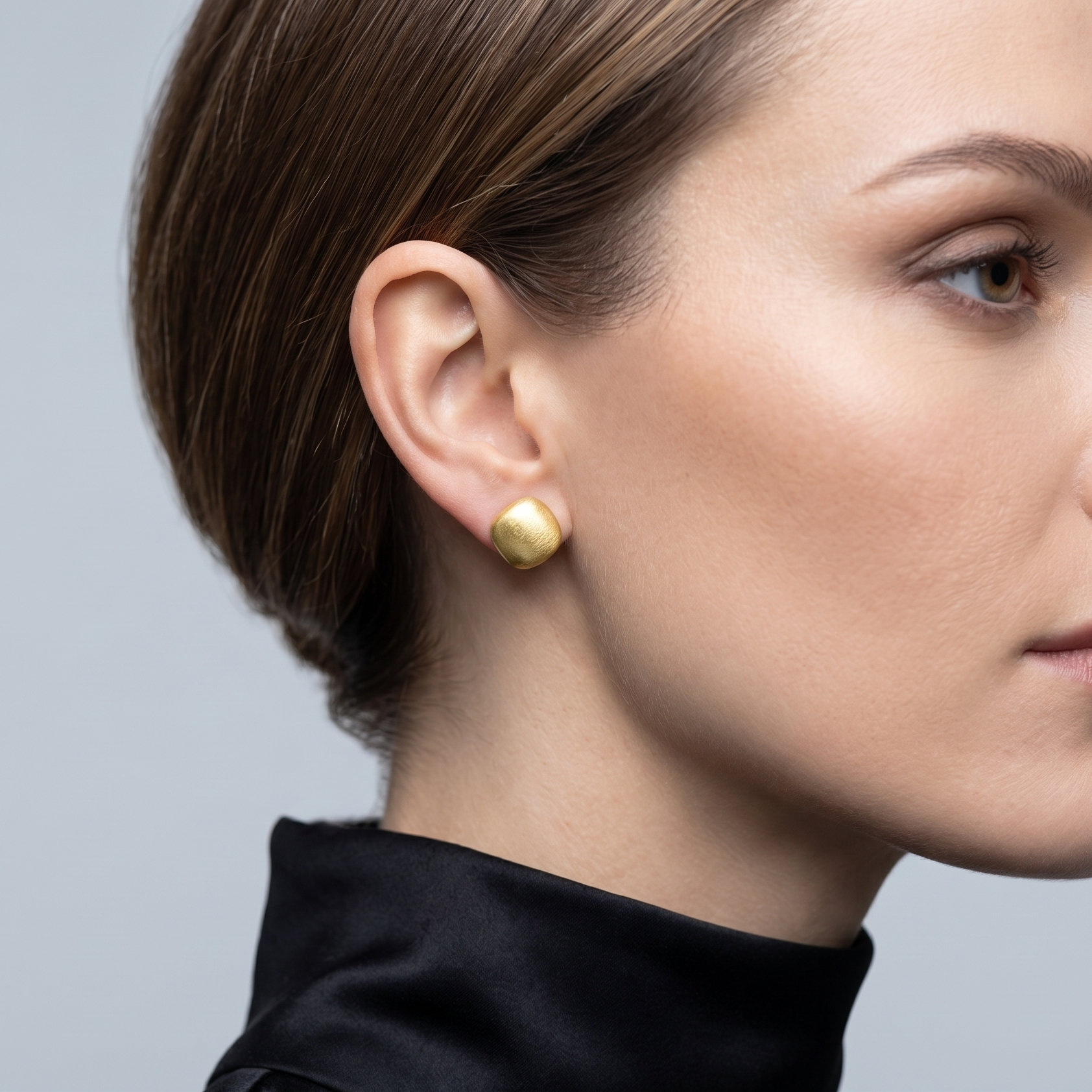 Close-up of a woman wearing gold earrings against a neutral background
