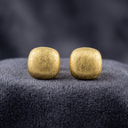 Pair of gold square earrings on a dark textured surface