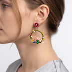 Close-up of a woman wearing a floral hoop earring with small figures on a plain background