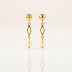 A pair of gold dangle earrings with a spherical stud, an open diamond-shaped link, and a hanging pearl, displayed on a clean white reflective surface.