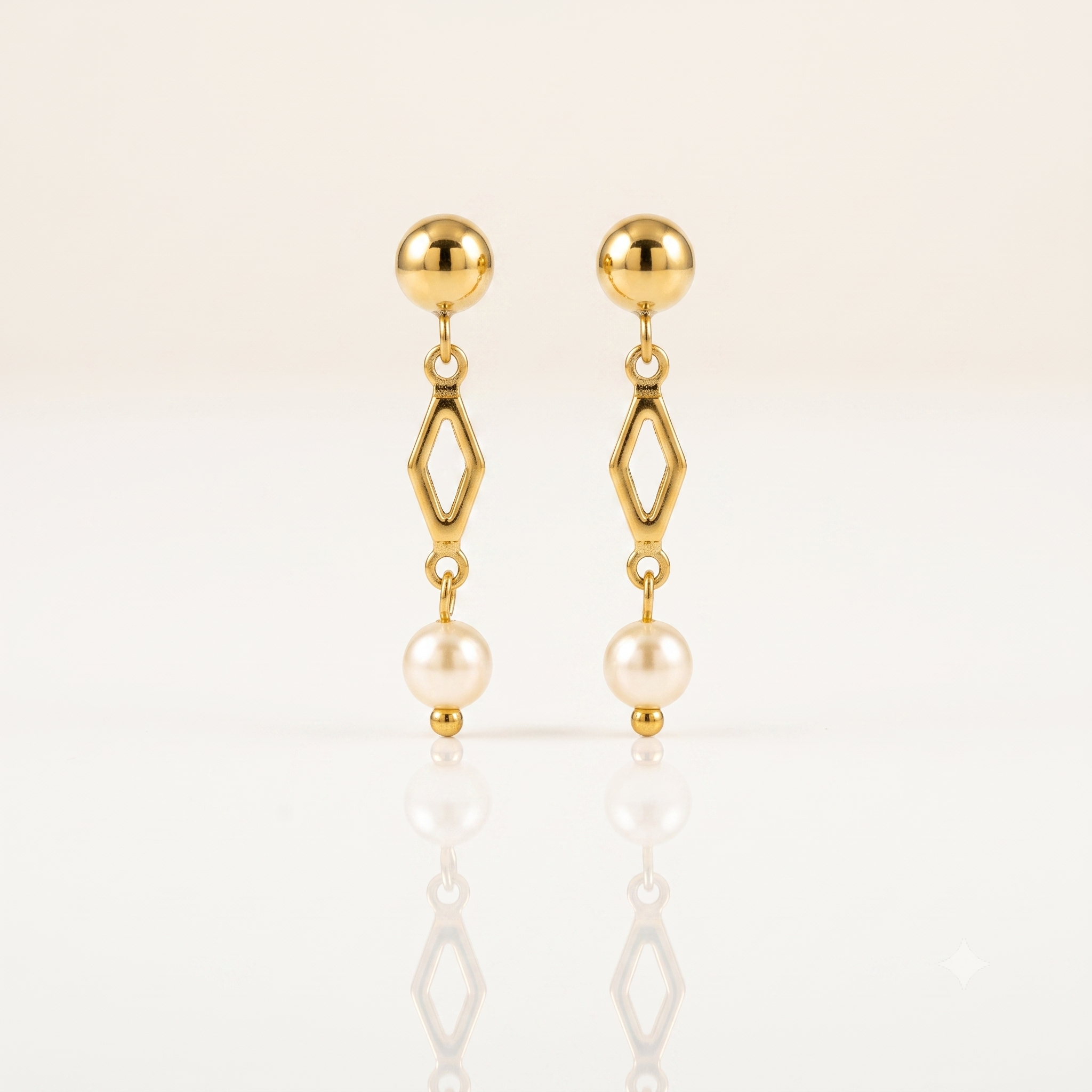 A pair of gold dangle earrings with a spherical stud, an open diamond-shaped link, and a hanging pearl, displayed on a clean white reflective surface.