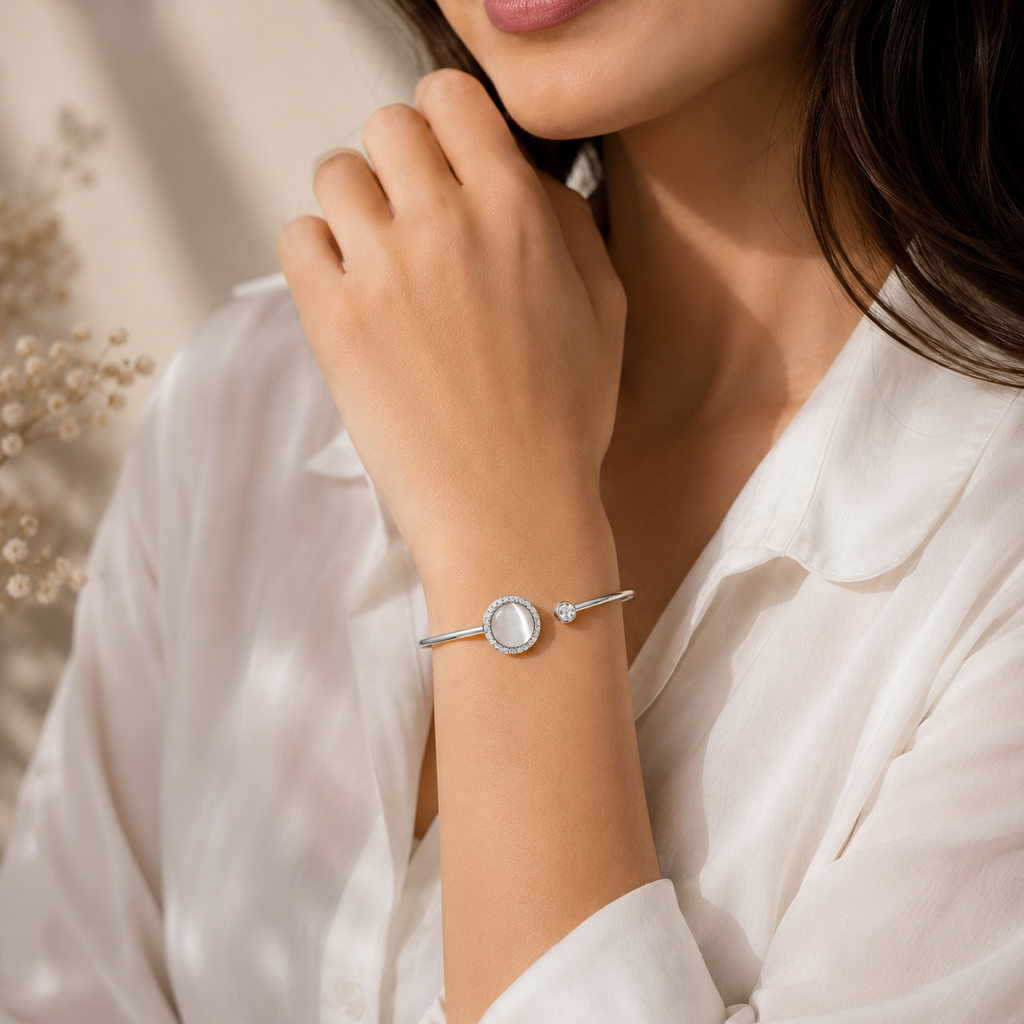 A close-up lifestyle shot of a woman wearing a delicate silver bangle bracelet with a central round white stone, styled with a white satin shirt.