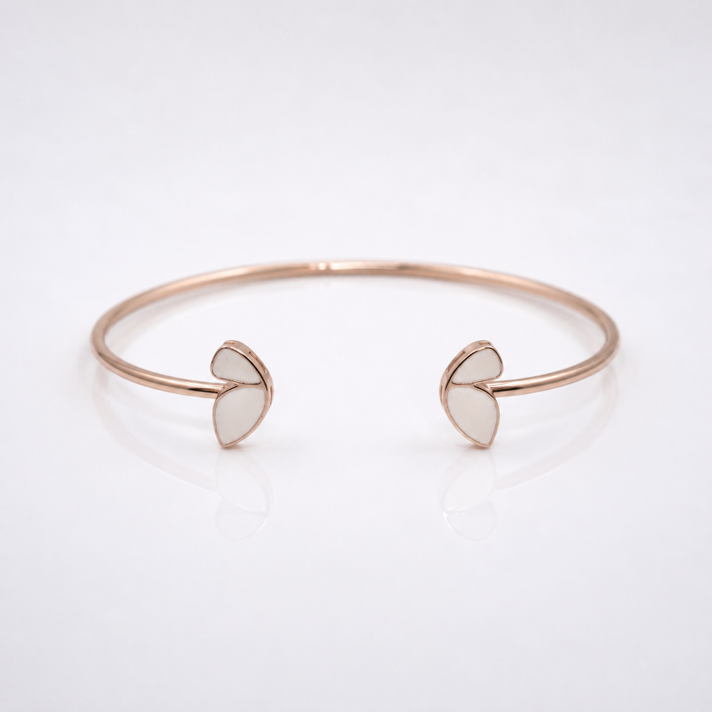 A minimalist rose gold cuff bracelet with two small open heart-shaped inlays on each end, displayed on a clean white reflective surface.