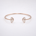 A minimalist rose gold cuff bracelet with two small open heart-shaped inlays on each end, displayed on a clean white reflective surface.