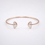 A minimalist rose gold cuff bracelet with two small open heart-shaped inlays on each end, displayed on a clean white reflective surface.