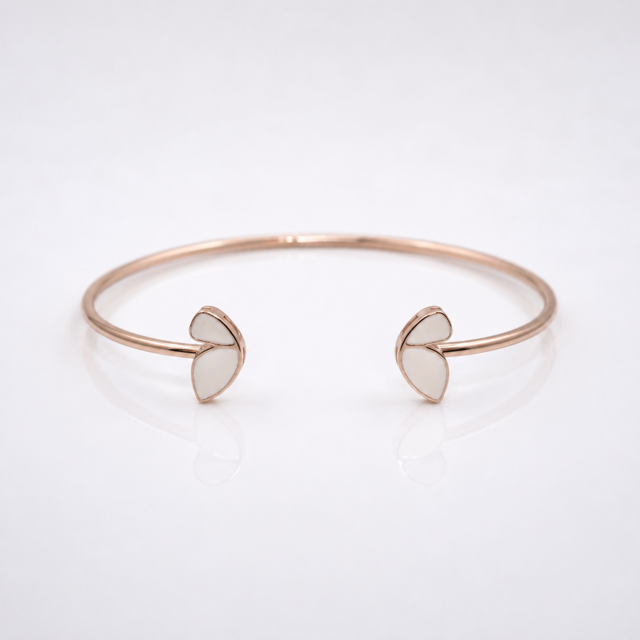 A minimalist rose gold cuff bracelet with two small open heart-shaped inlays on each end, displayed on a clean white reflective surface.