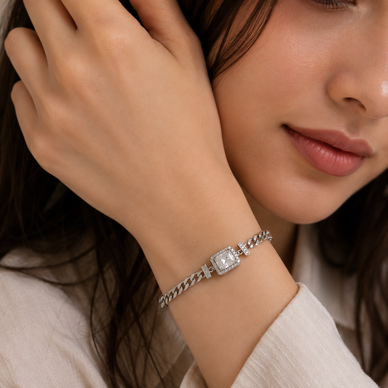 A close-up lifestyle shot of a woman wearing a silver-toned chain bracelet with a square bezel-set clear gemstone on her wrist.