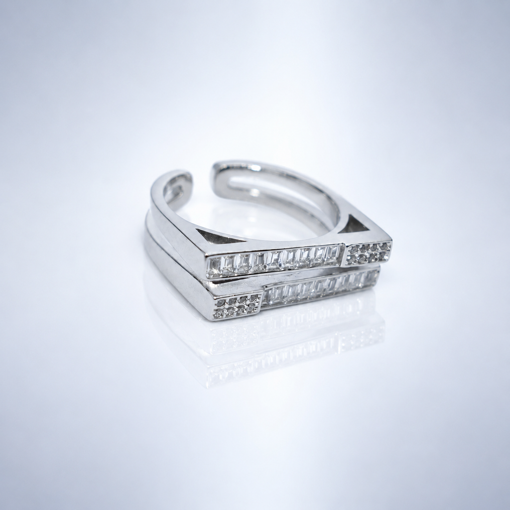 A silver-toned open band ring featuring two parallel rectangular bars set with clear baguette gemstones, photographed on a clean white reflective surface.