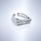 A silver-toned open band ring featuring two parallel rectangular bars set with clear baguette gemstones, photographed on a clean white reflective surface.