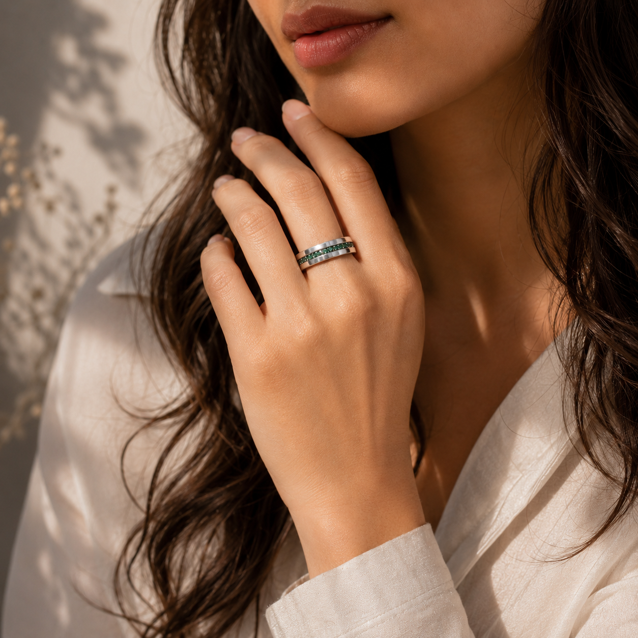 A close-up lifestyle shot of a woman wearing a silver band ring with a row of small round blue gemstones, set against a warm, softly lit background.