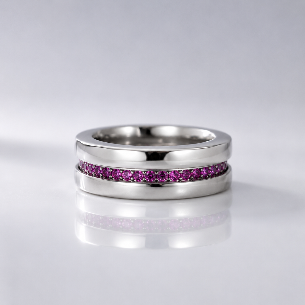 A polished silver-tone ring featuring a channel-set row of small pink gemstones, displayed on a reflective light gray surface.